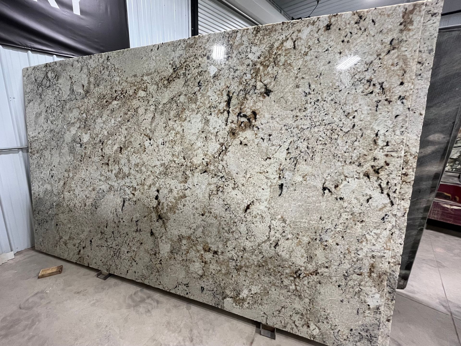 A large slab of polished granite featuring a white, beige, and gray mottled pattern with dark speckles.