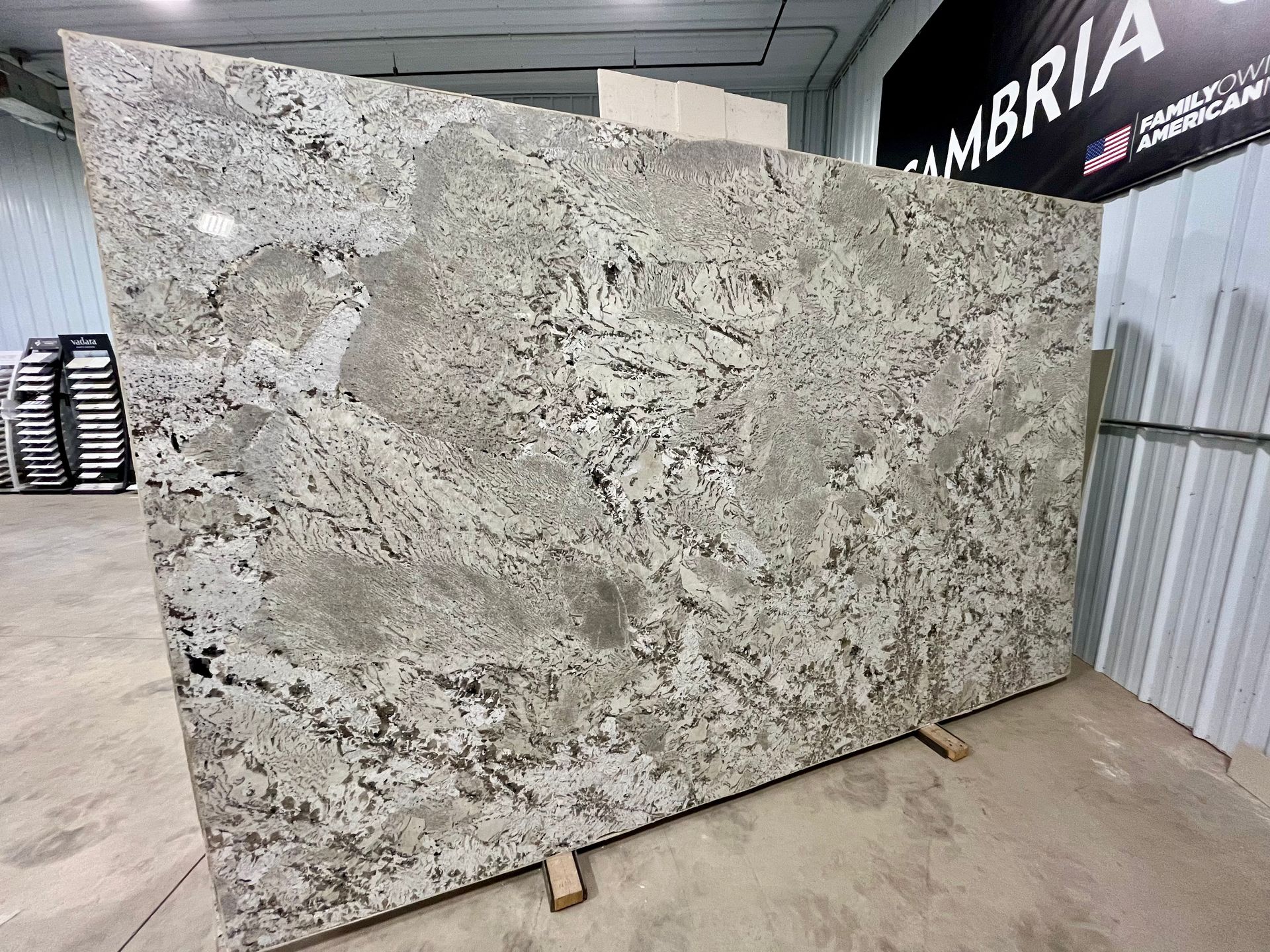 A large slab of white, grey, and black granite standing on wooden supports inside a warehouse.