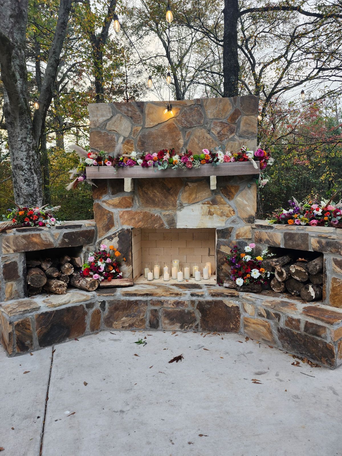 A stone fireplace decorated with flowers and candles.