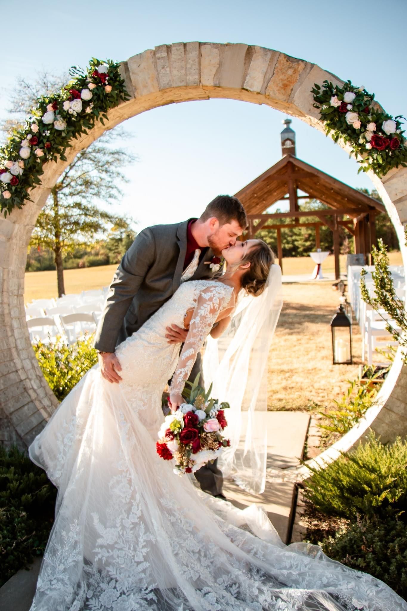 A bride and groom are kissing under a stone arch at their wedding.