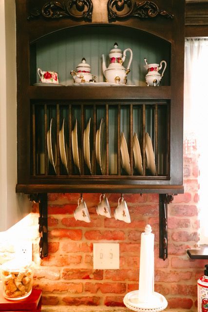 A kitchen with a brick wall and a shelf with plates and cups on it
