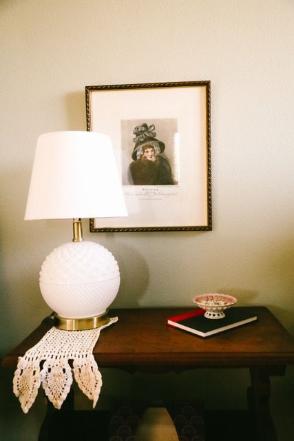 A lamp is sitting on a table next to a picture on the wall.