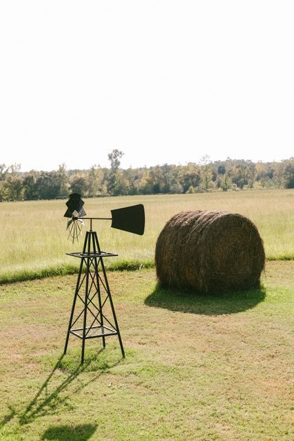 A windmill and a bale of hay are in a field.