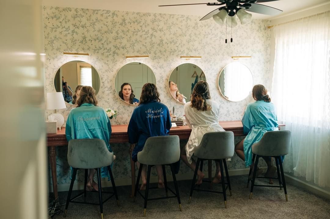 A group of women are sitting in front of mirrors in a dressing room.