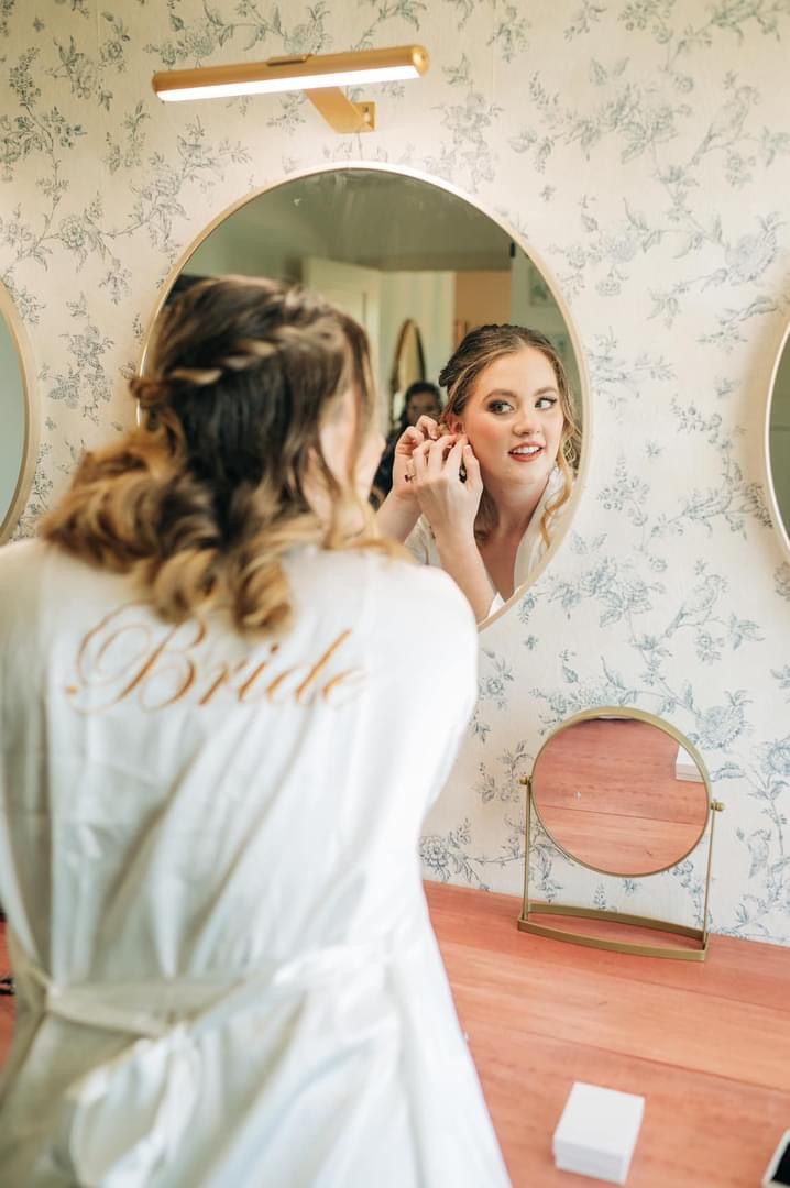 A woman in a white robe is looking at herself in a mirror.