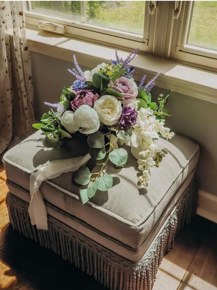 A bouquet of flowers is sitting on an ottoman in front of a window.