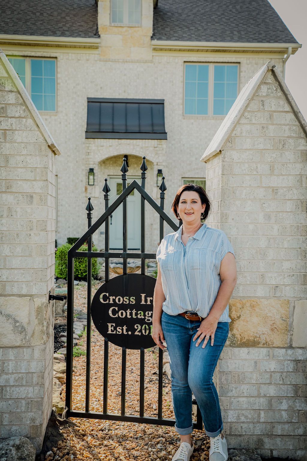 A woman is standing in front of a house next to a gate.