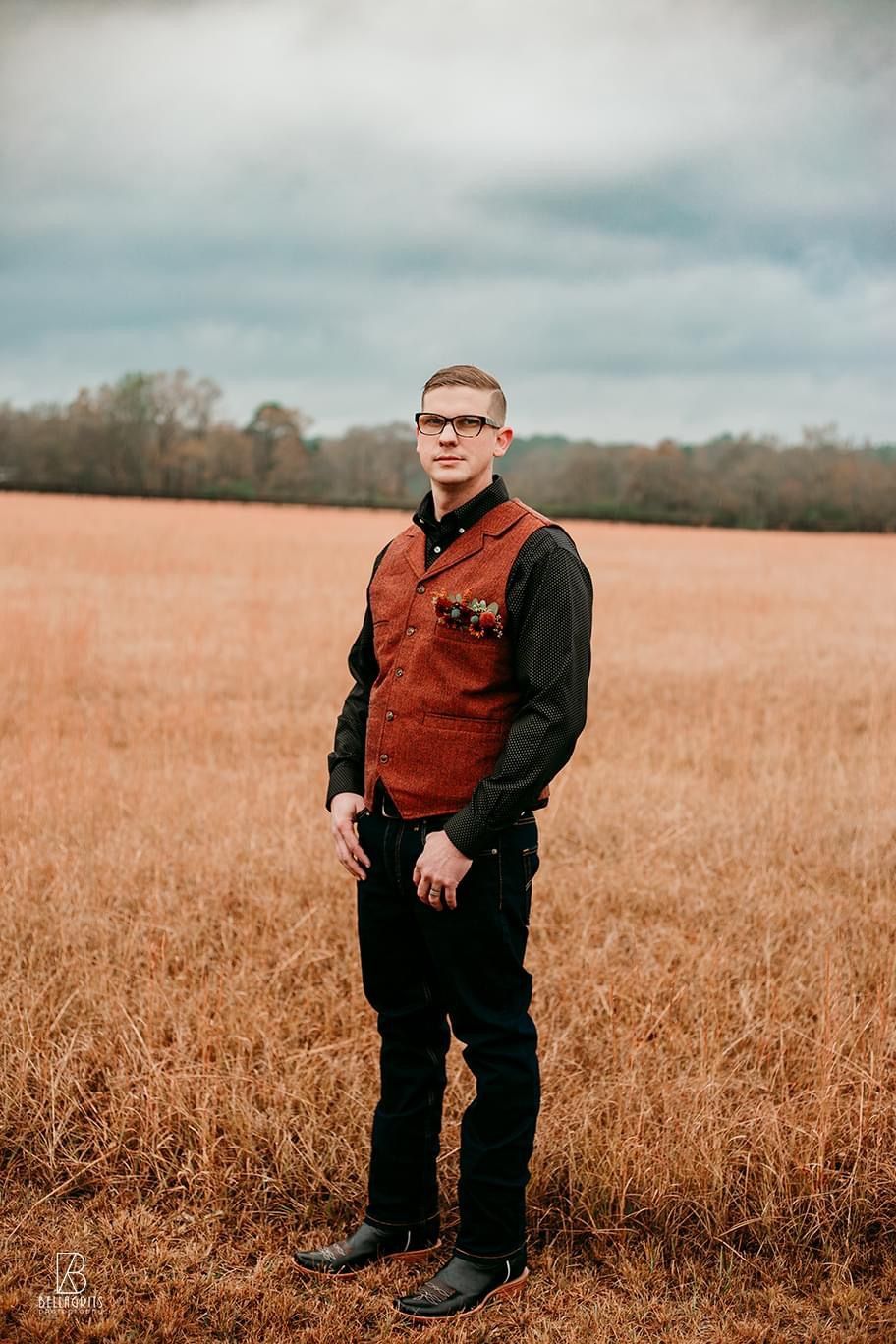 A man in a red vest is standing in a field.