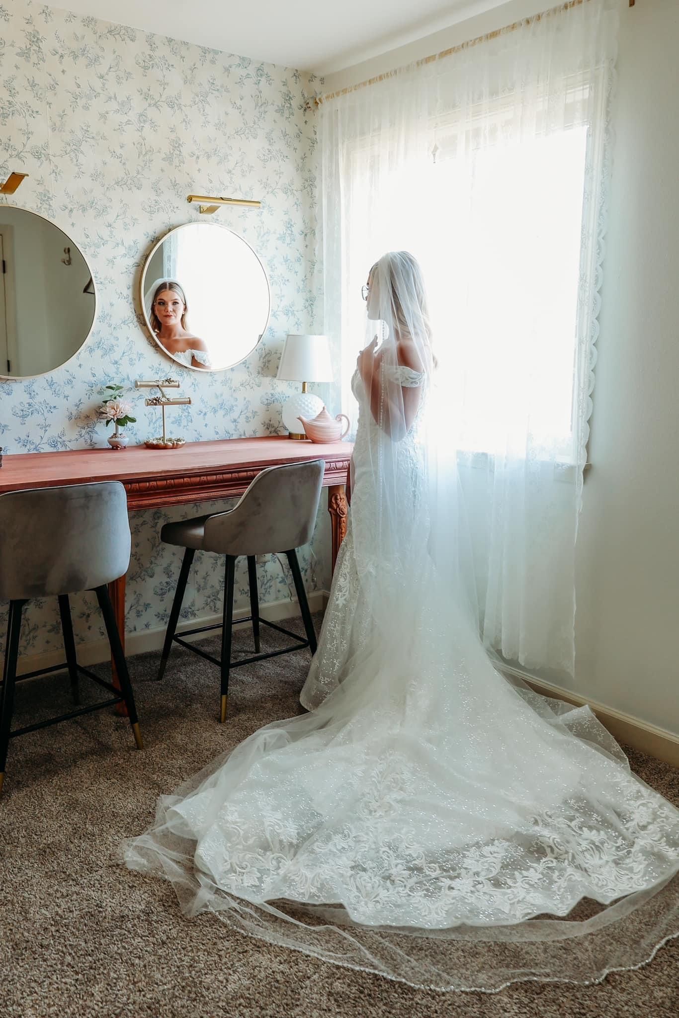 A bride in a wedding dress is standing in front of a mirror in a room.