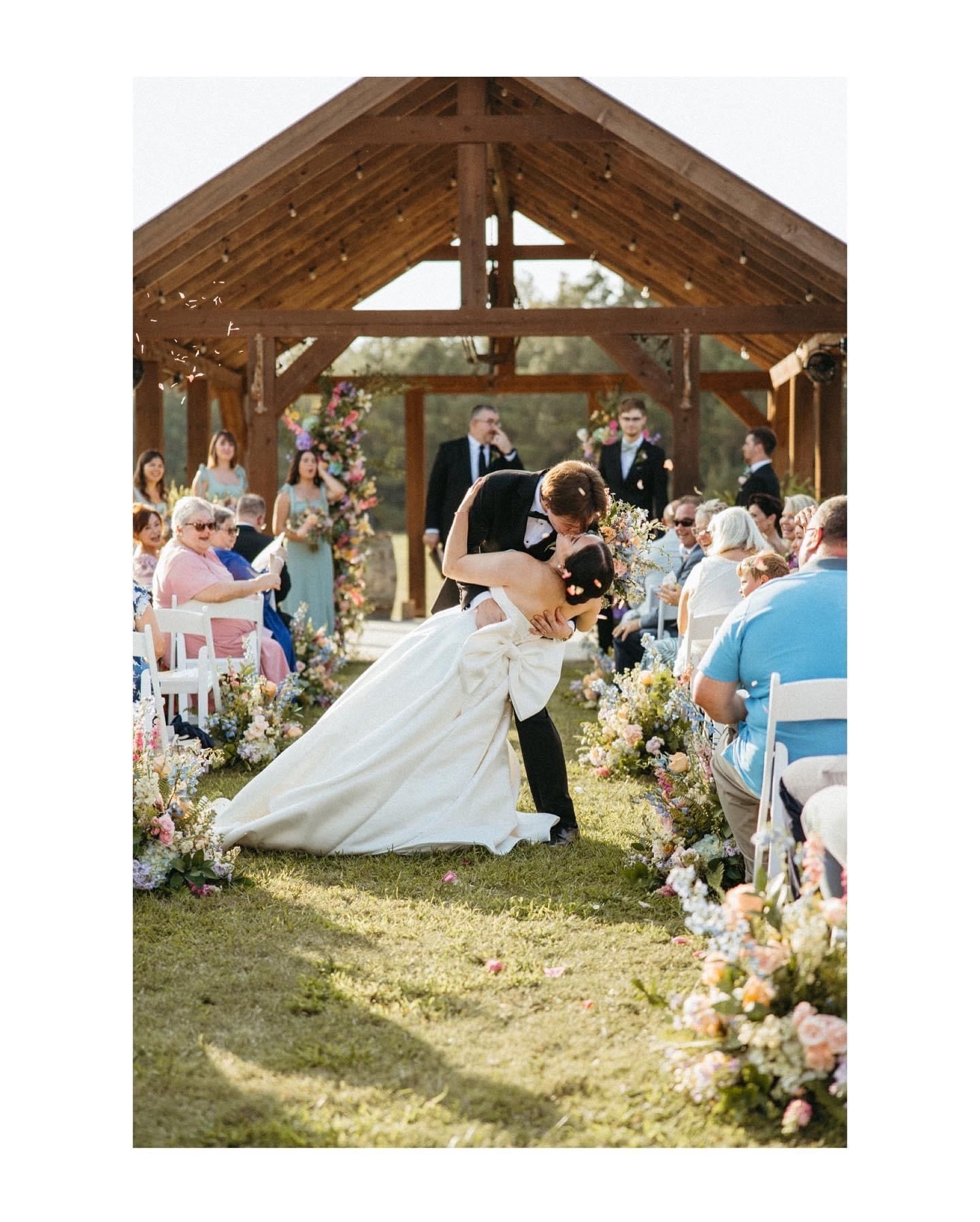 A bride and groom are kissing at their wedding under a wooden structure.