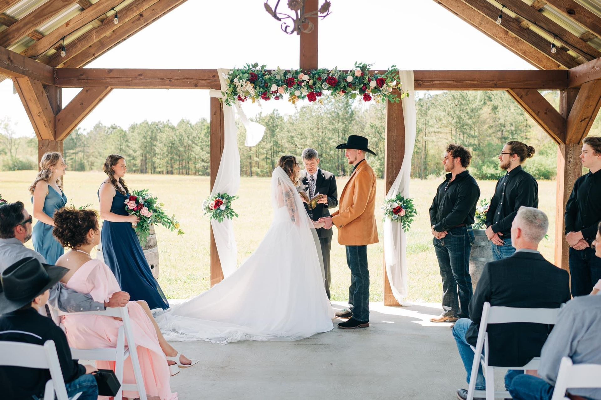 A bride and groom are holding hands during their wedding ceremony under a gazebo.