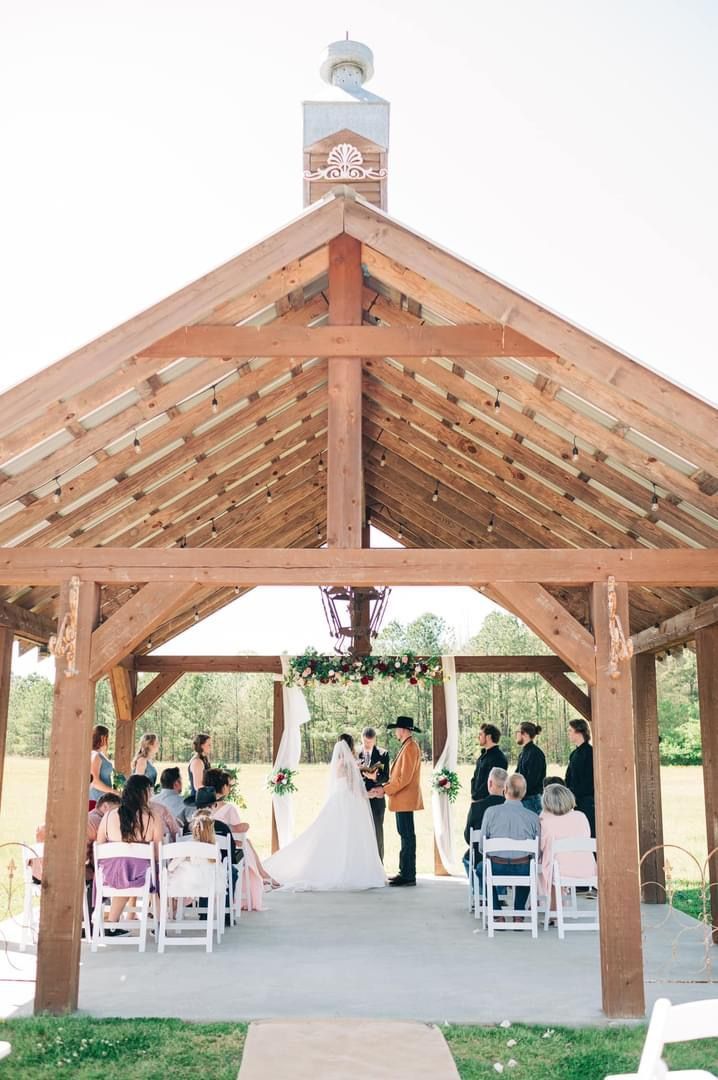 A bride and groom are getting married under a wooden pavilion.