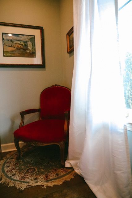 A red chair is sitting in a corner of a room next to a window.