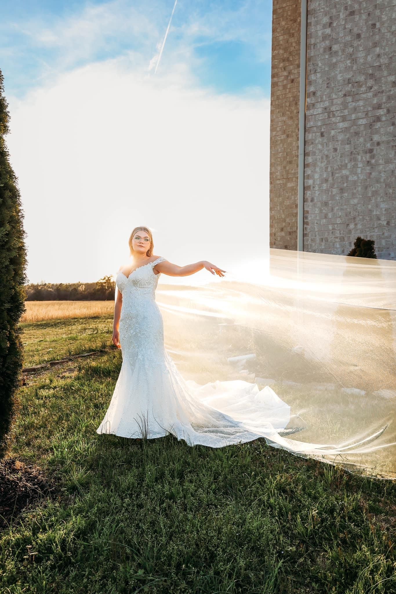 A bride in a wedding dress is standing in the grass in front of a building.