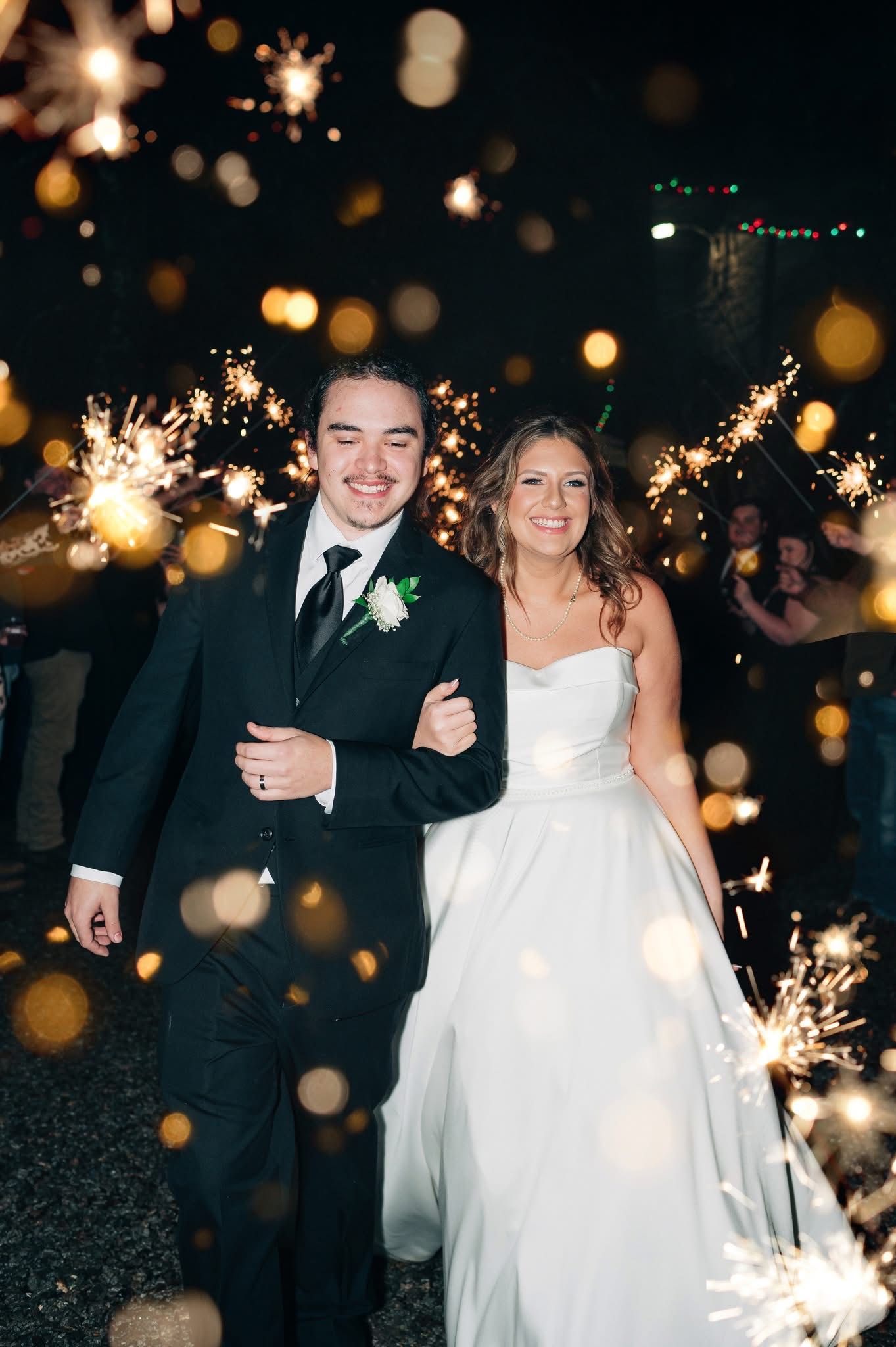 A bride and groom are walking through a tunnel of sparklers.