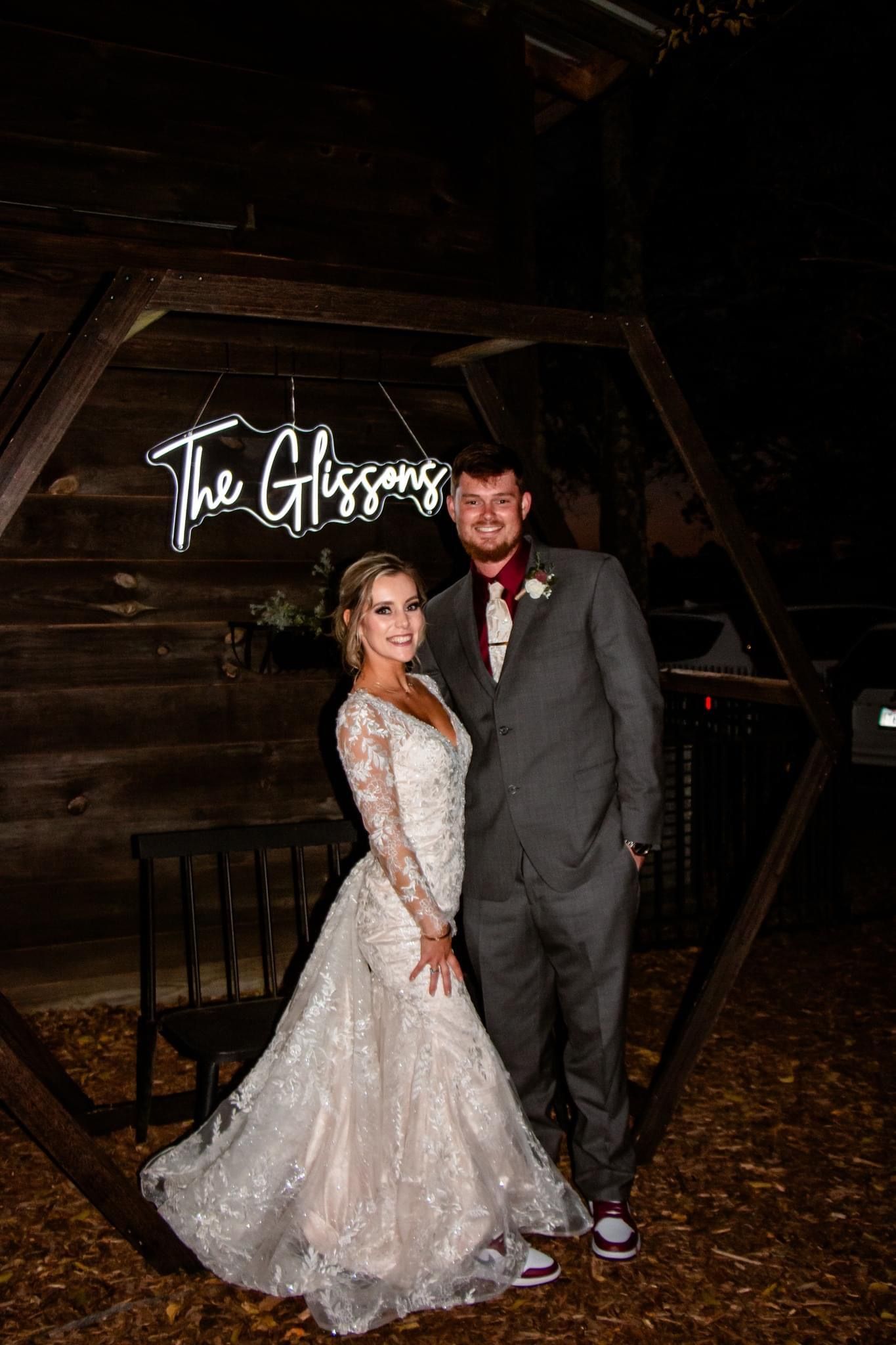 A bride and groom are posing for a picture in front of a neon sign.