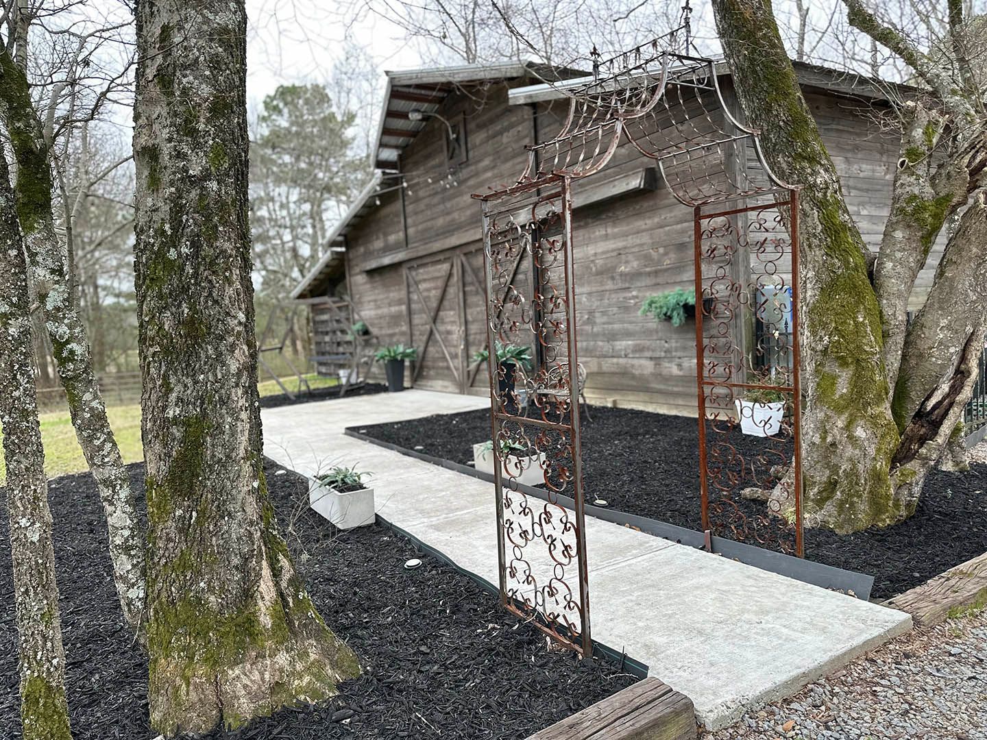 A wooden barn with a walkway leading to it surrounded by trees.