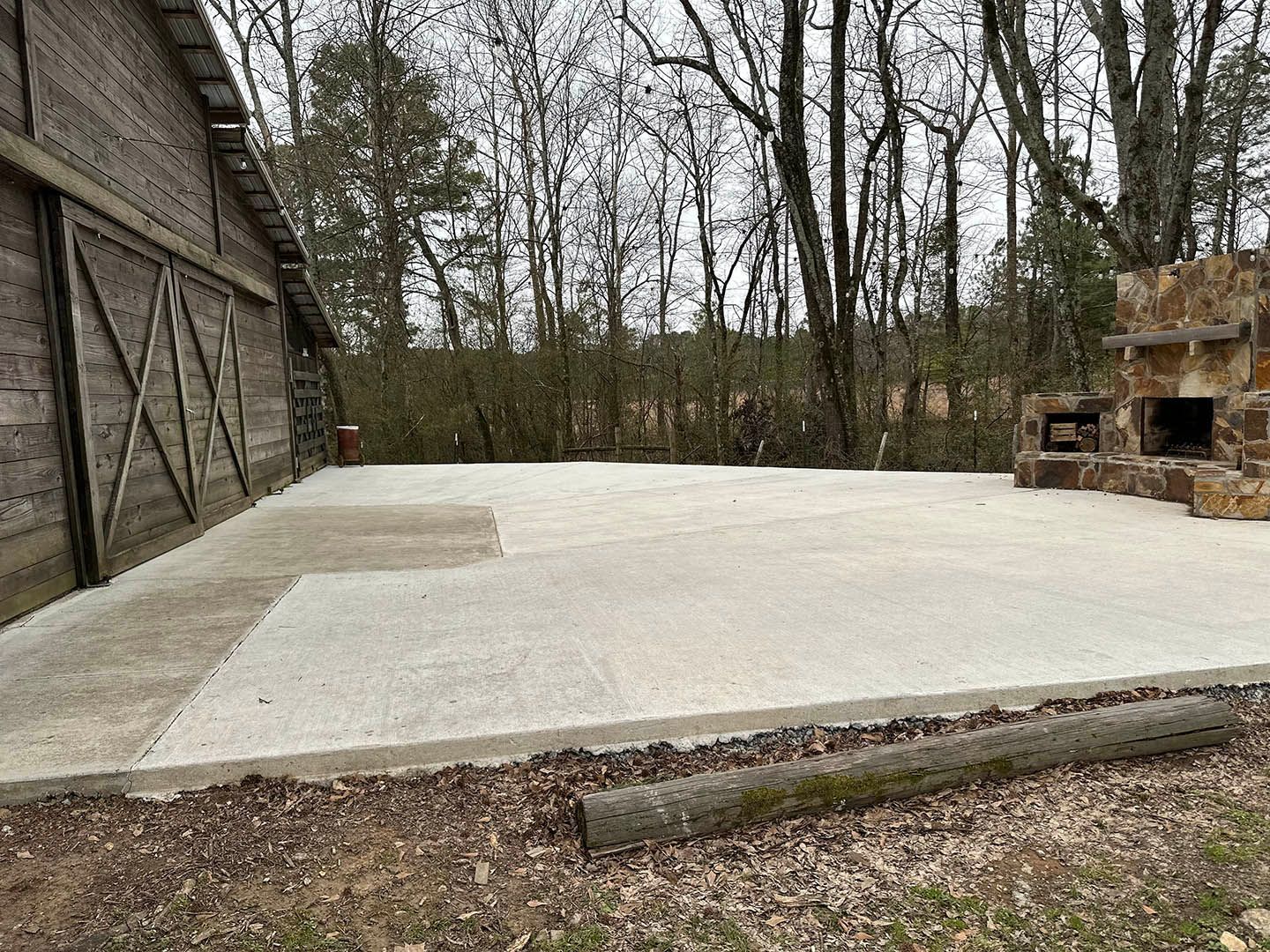 A concrete patio with a fireplace and a barn in the background.