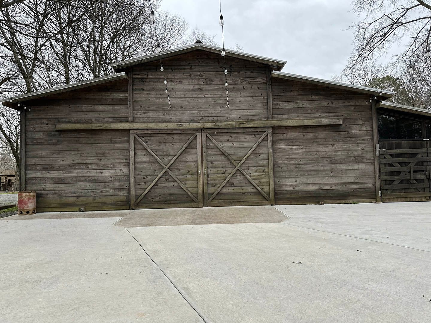 A large wooden barn with a concrete driveway in front of it.