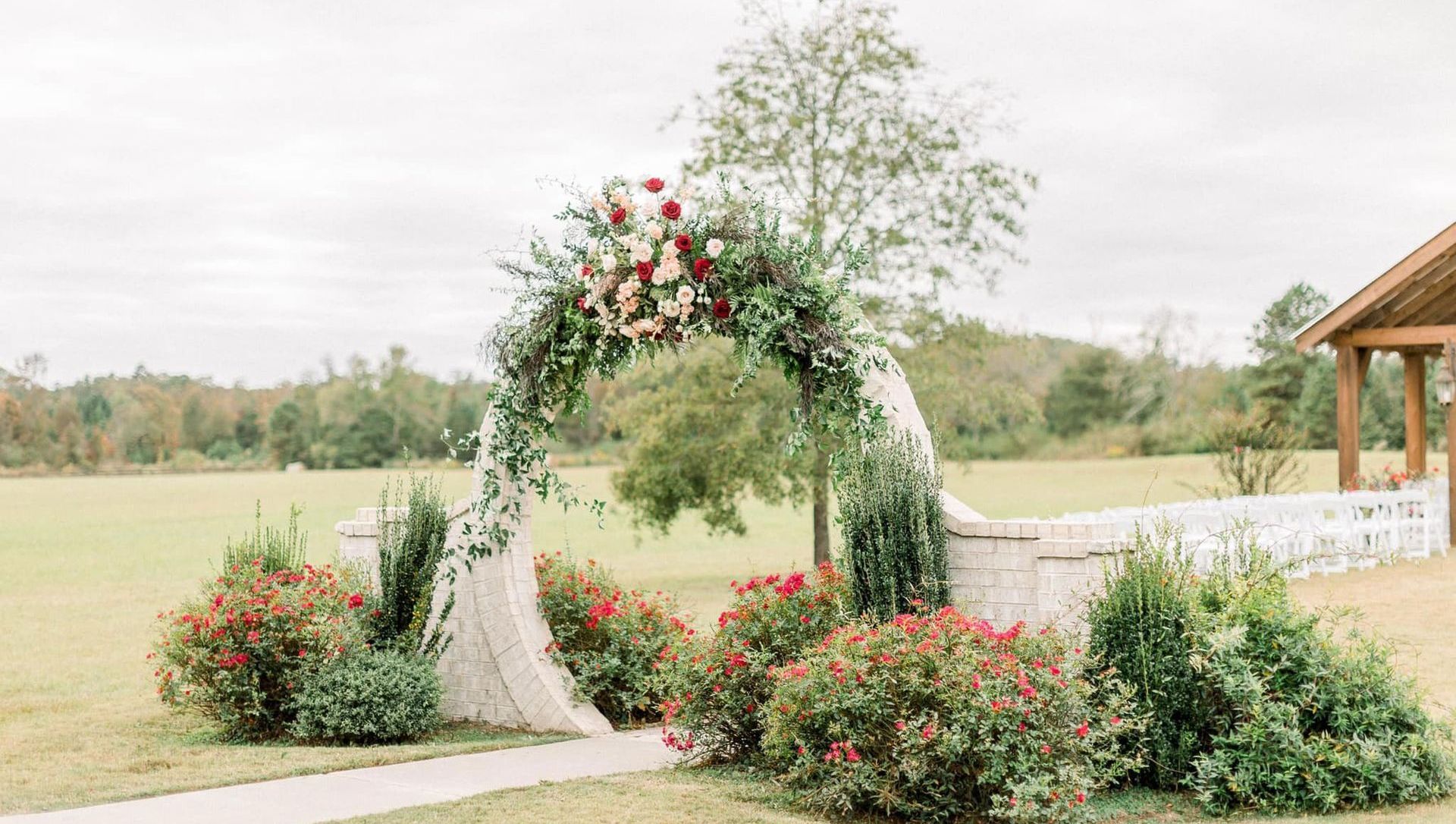 A bride and groom are standing under an arch decorated with flowers in a field.