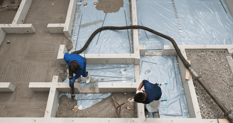 Two workers pouring concrete from hose and spreading it with rake