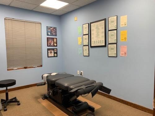 Chiropractic office examination room with a specialized treatment table, certificates, and a window with blinds.