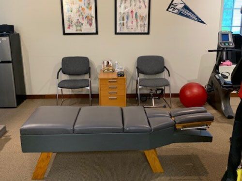 Chiropractic office with adjusting table, chairs, and exercise ball.