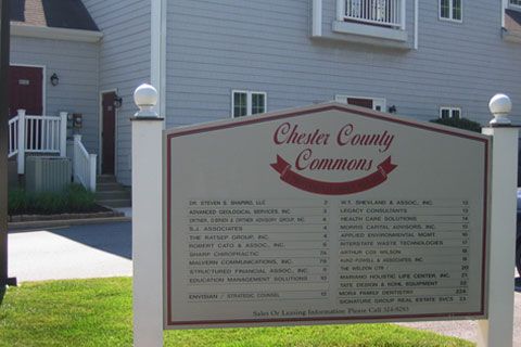 Sign for Chester County Commons with businesses listed. Blue building in background, green grass.