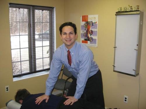 Chiropractor adjusting a patient's back in an office; window and an X-ray viewer in the background.