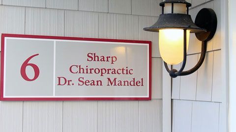 Sign for Sharp Chiropractic, Dr. Sean Mandel, building number 6, with a wall-mounted lamp.