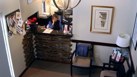 Reception area with stone-faced desk, person on phone, chairs, and framed art.