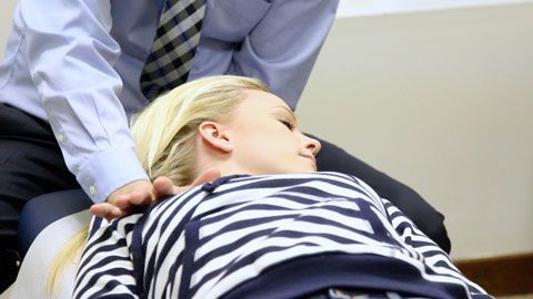 Chiropractor adjusting a person's neck. Person laying down, eyes closed.