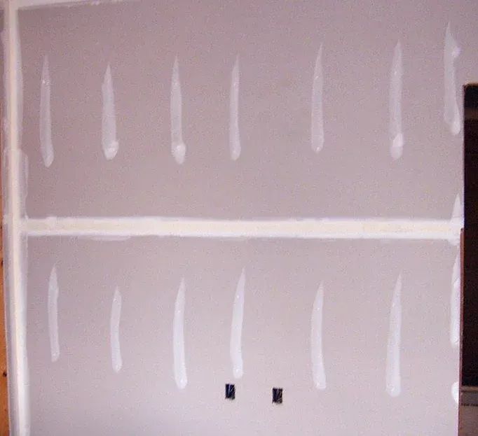 Gray drywall with white joint compound applied in vertical lines and along seams.