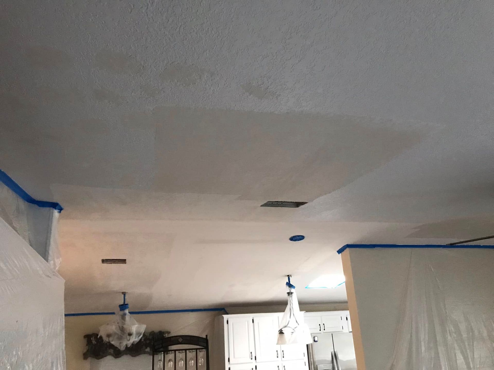 Ceiling with water stains being repaired, covered in painter's tape and plastic sheeting.