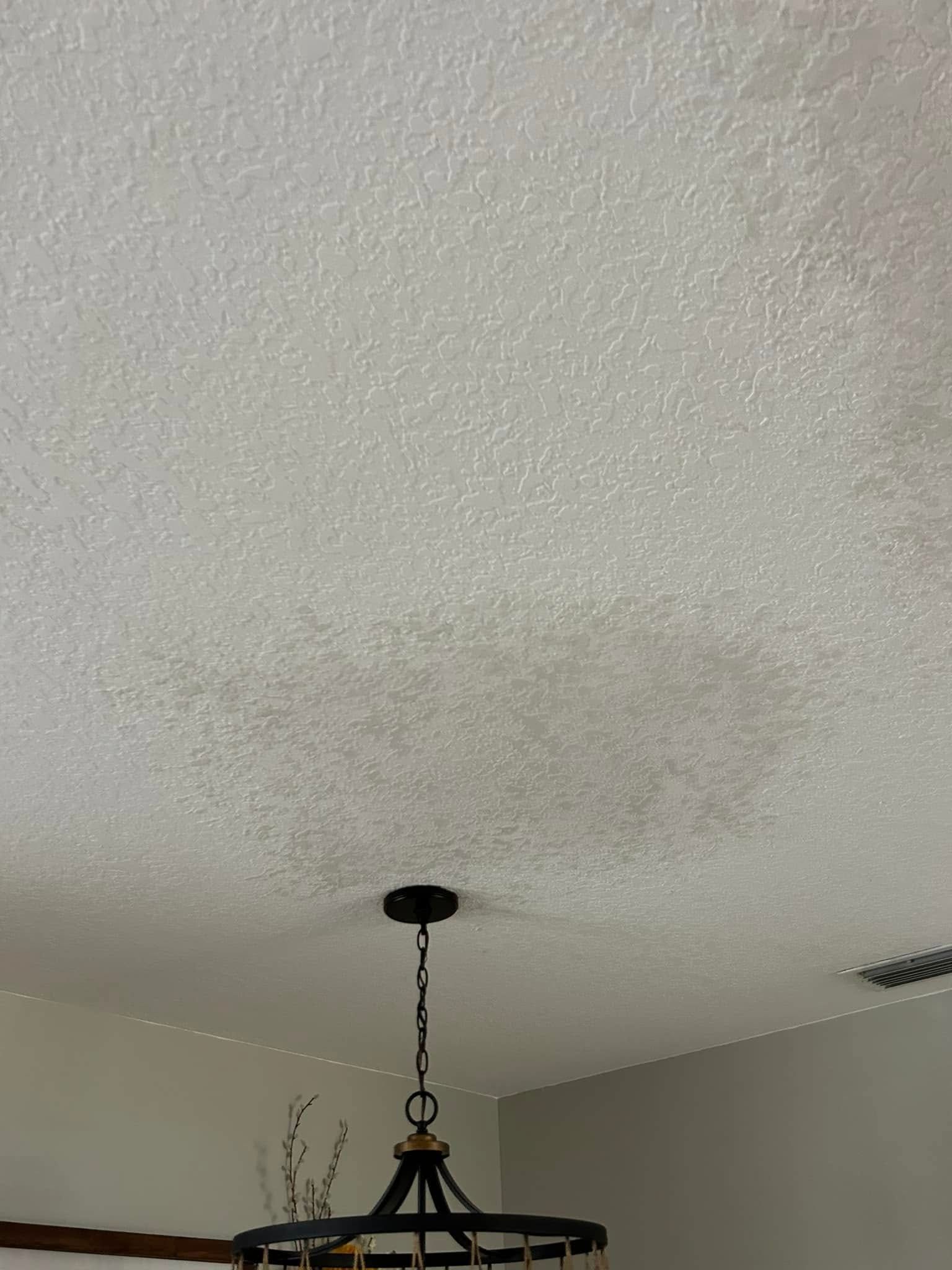 White textured ceiling with a dark chandelier hanging below.