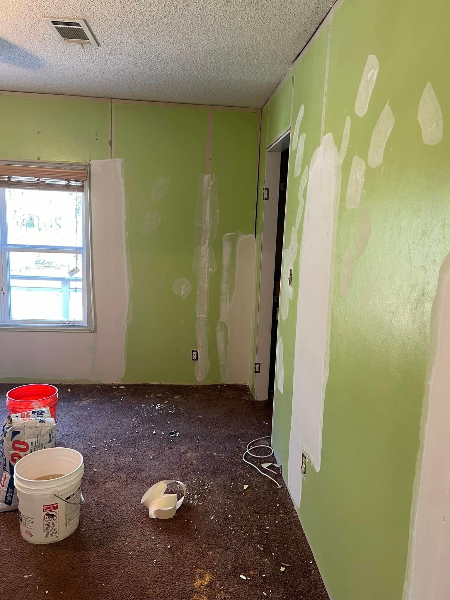 Room interior under construction with green walls, white patches, and scattered debris on the floor.