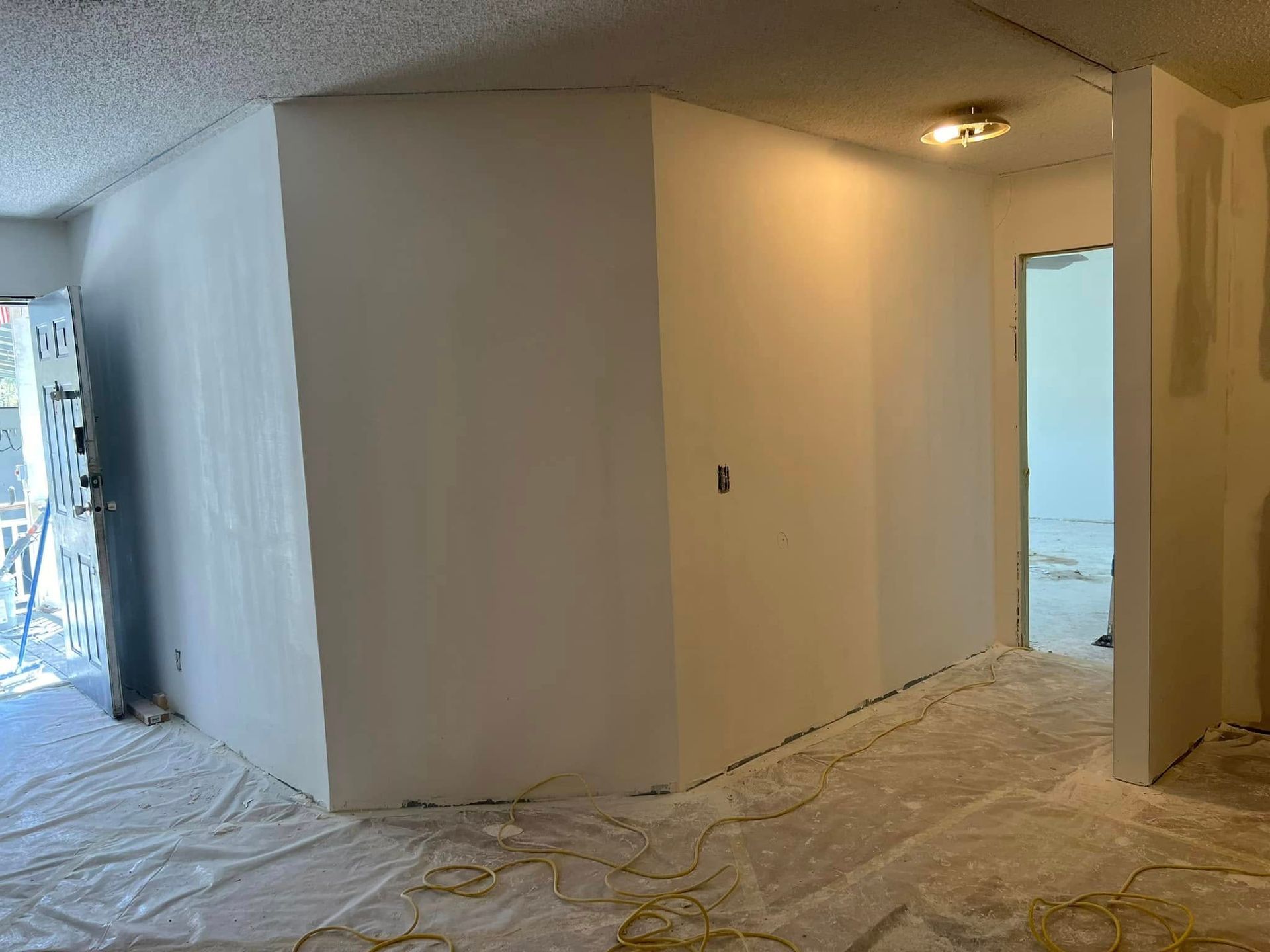 Interior view of a room with freshly painted walls, door, and doorway; work in progress, covered floors.