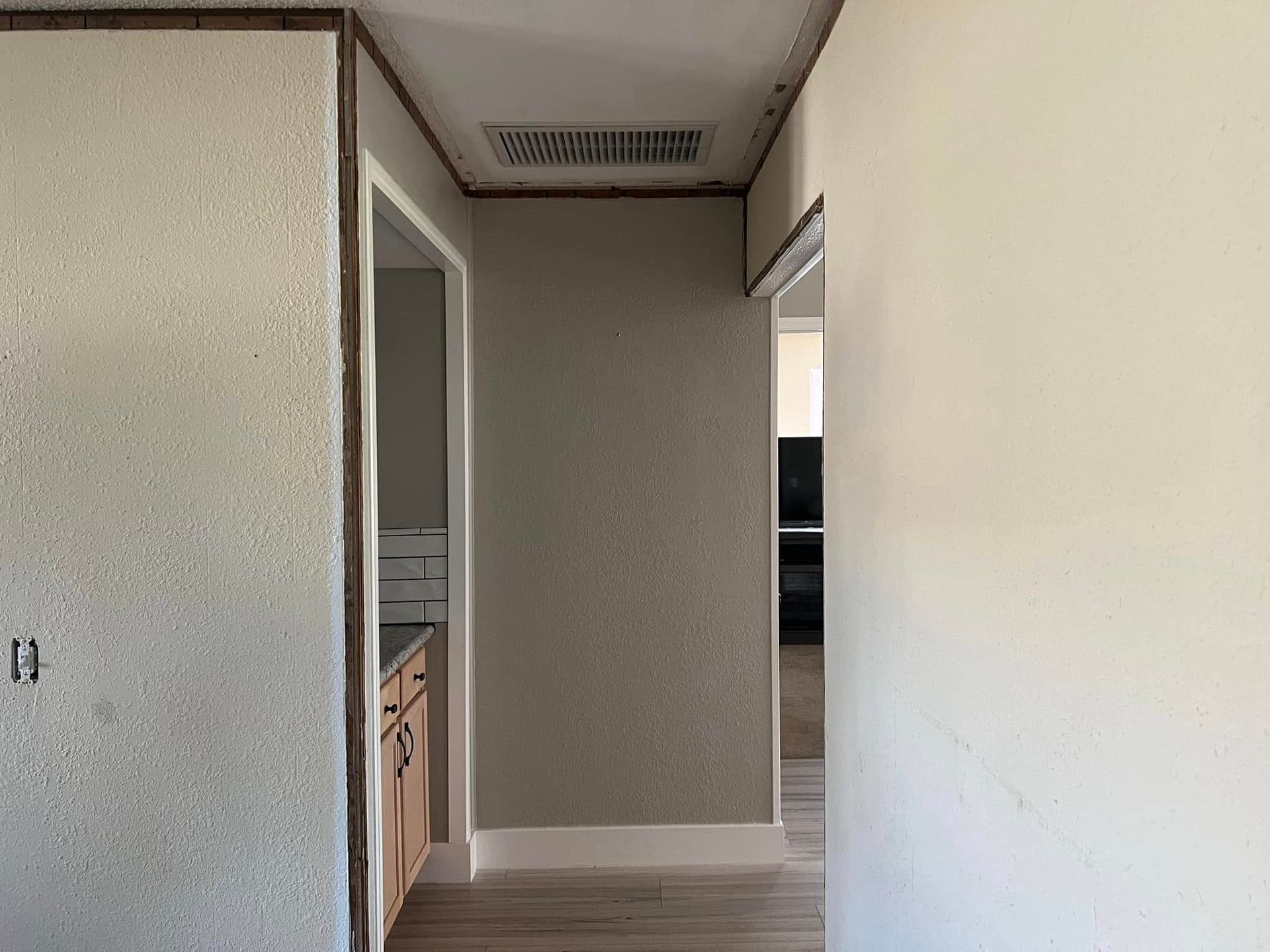 Hallway with textured gray walls, opening to a kitchen and a room with cabinets.