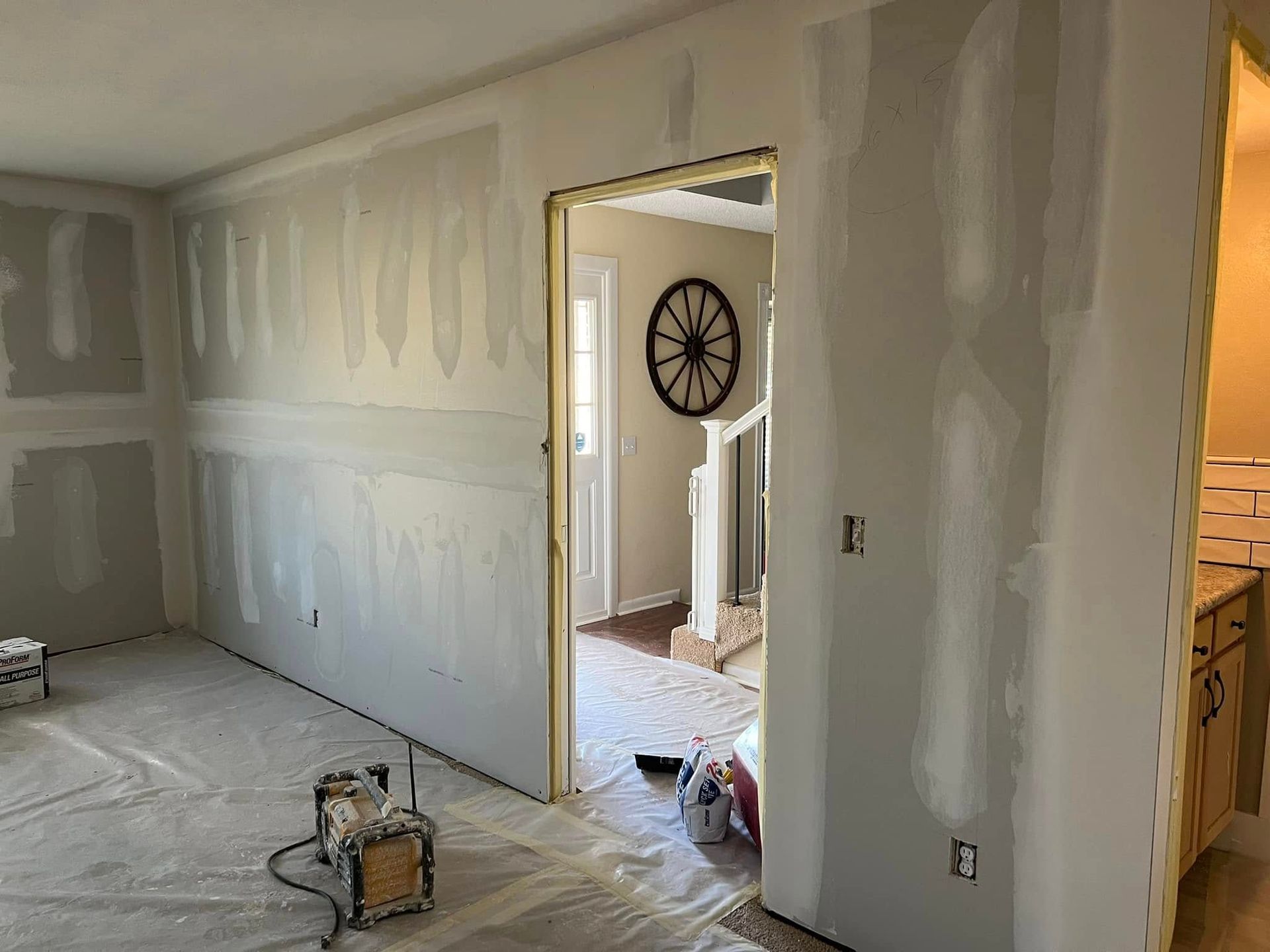 Room under construction with drywall installed; doorway leads to another room with a clock and fireplace.
