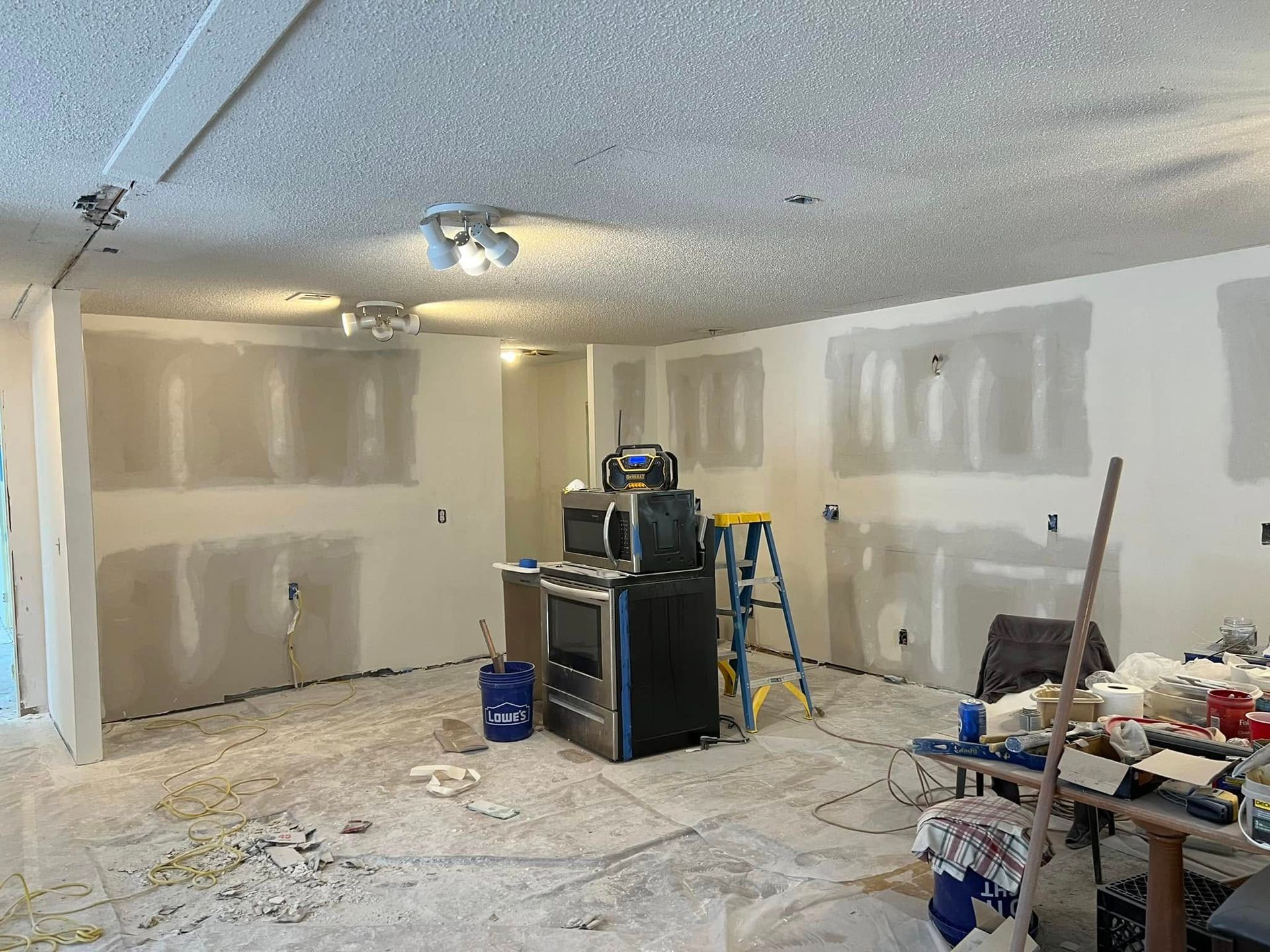 Interior room under construction, drywall on walls, stove, microwave, ladder, and debris on the floor.