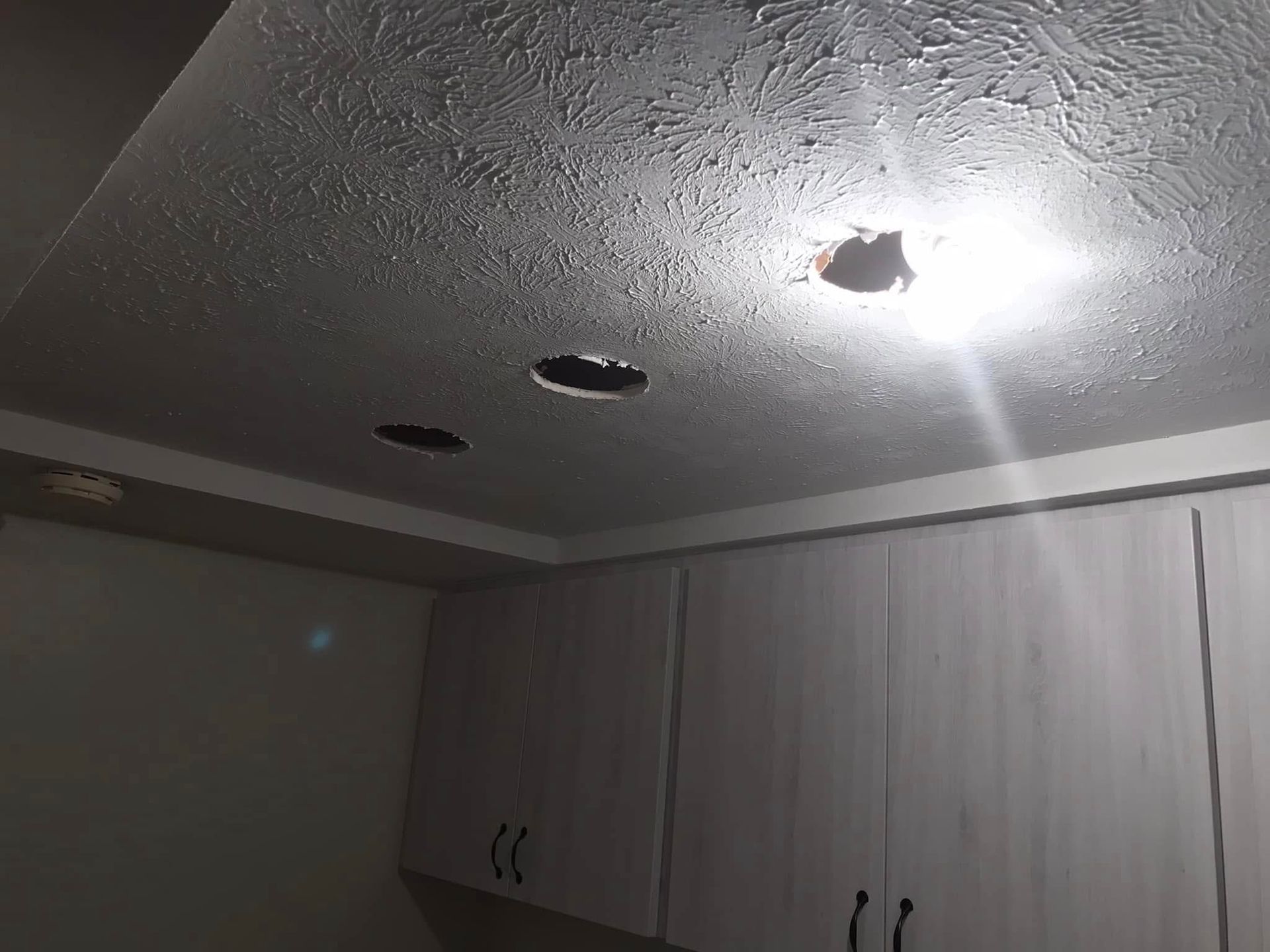 Ceiling with three holes cut out, above cabinets, possibly for recessed lighting.