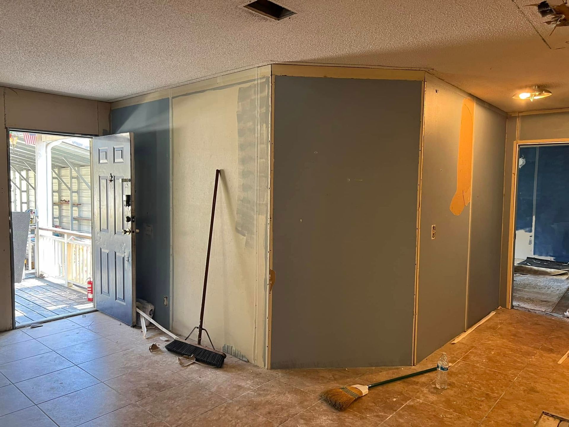 Interior renovation with unfinished walls and exposed drywall, broom, and doorway to the outside.