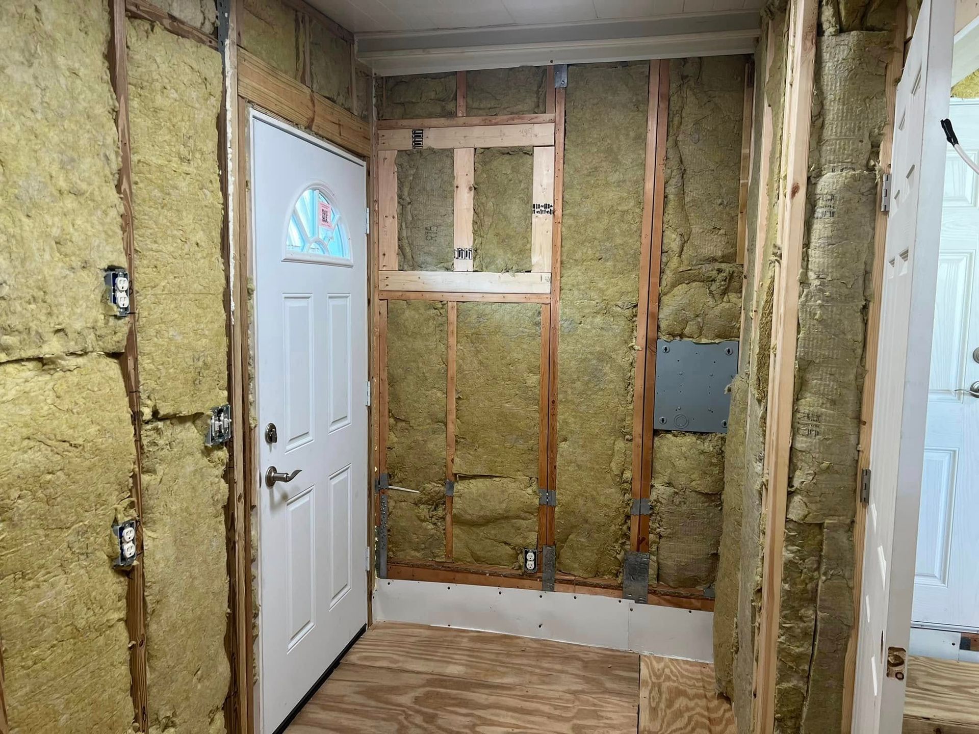Interior doorway with exposed framing, insulation, electrical boxes, and a white door.