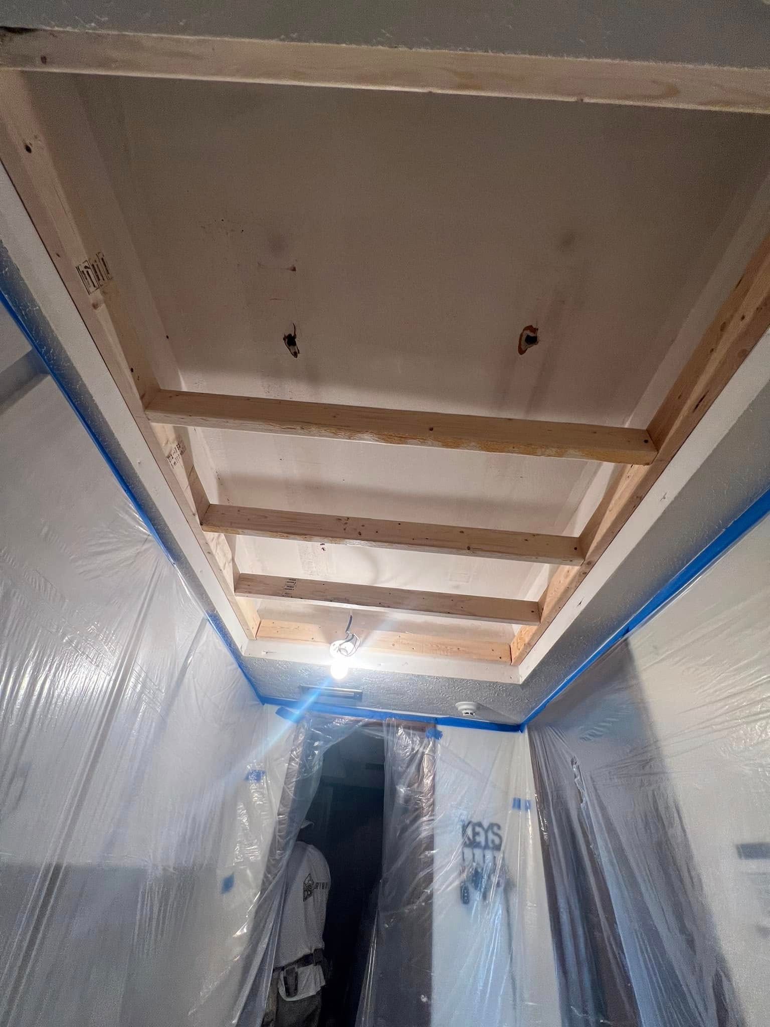 Wooden frame construction on a ceiling in a hallway. Walls are covered in plastic sheeting.