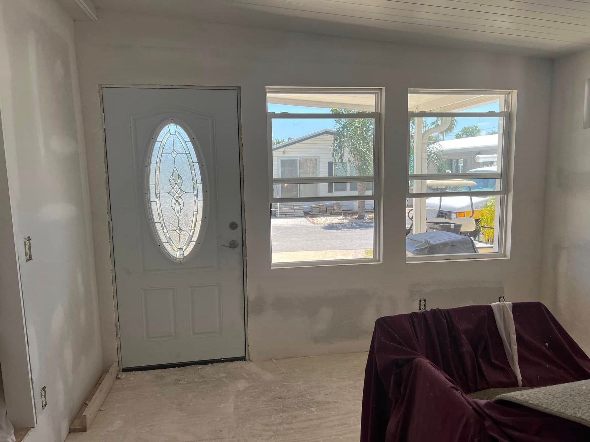 Interior view of a room with a white door with an oval window and two windows. A couch is covered in burgundy fabric.