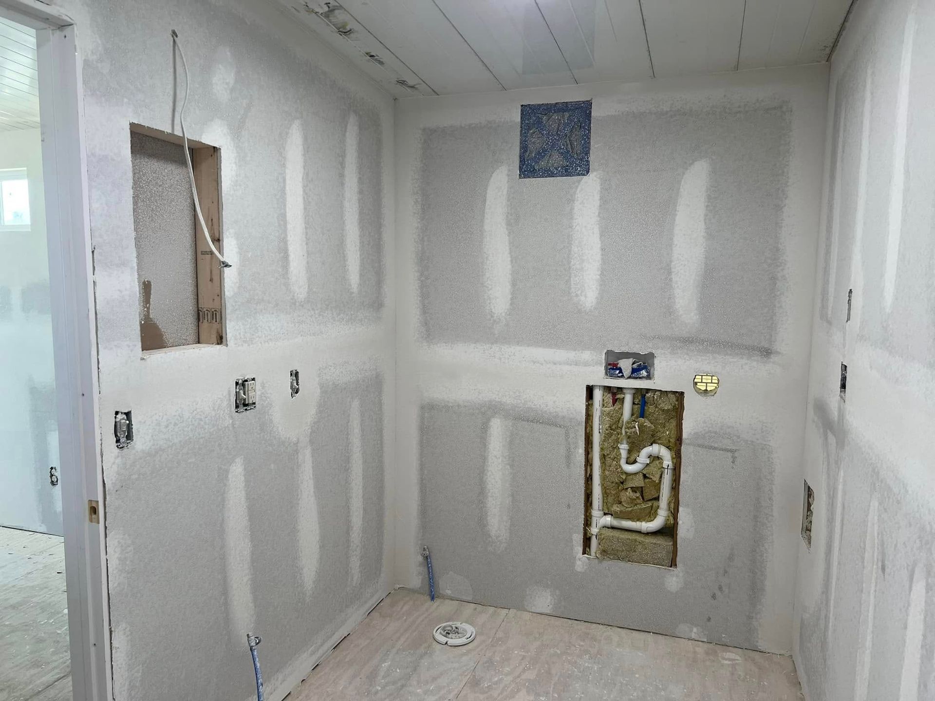 Unfinished bathroom with drywall, exposed wiring and plumbing, and electrical outlets.