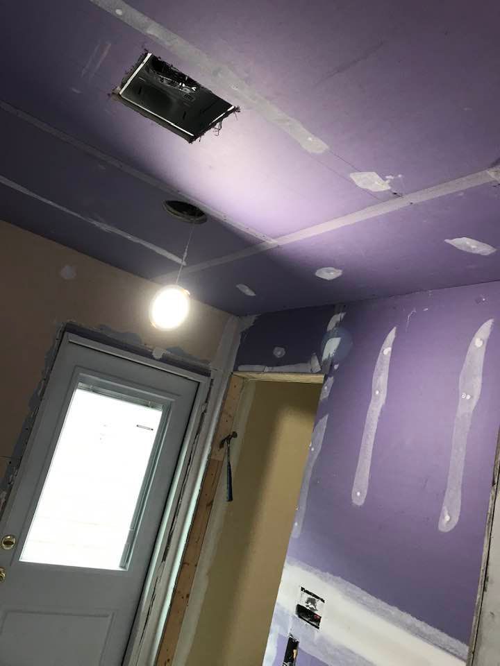 Purple drywall ceiling and walls in a room under construction, with a door and vent.