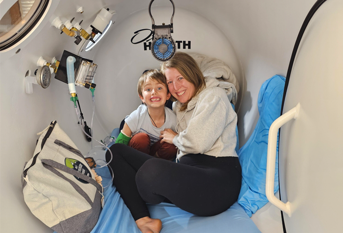 A man is sitting in an oxygen chamber on a bed.