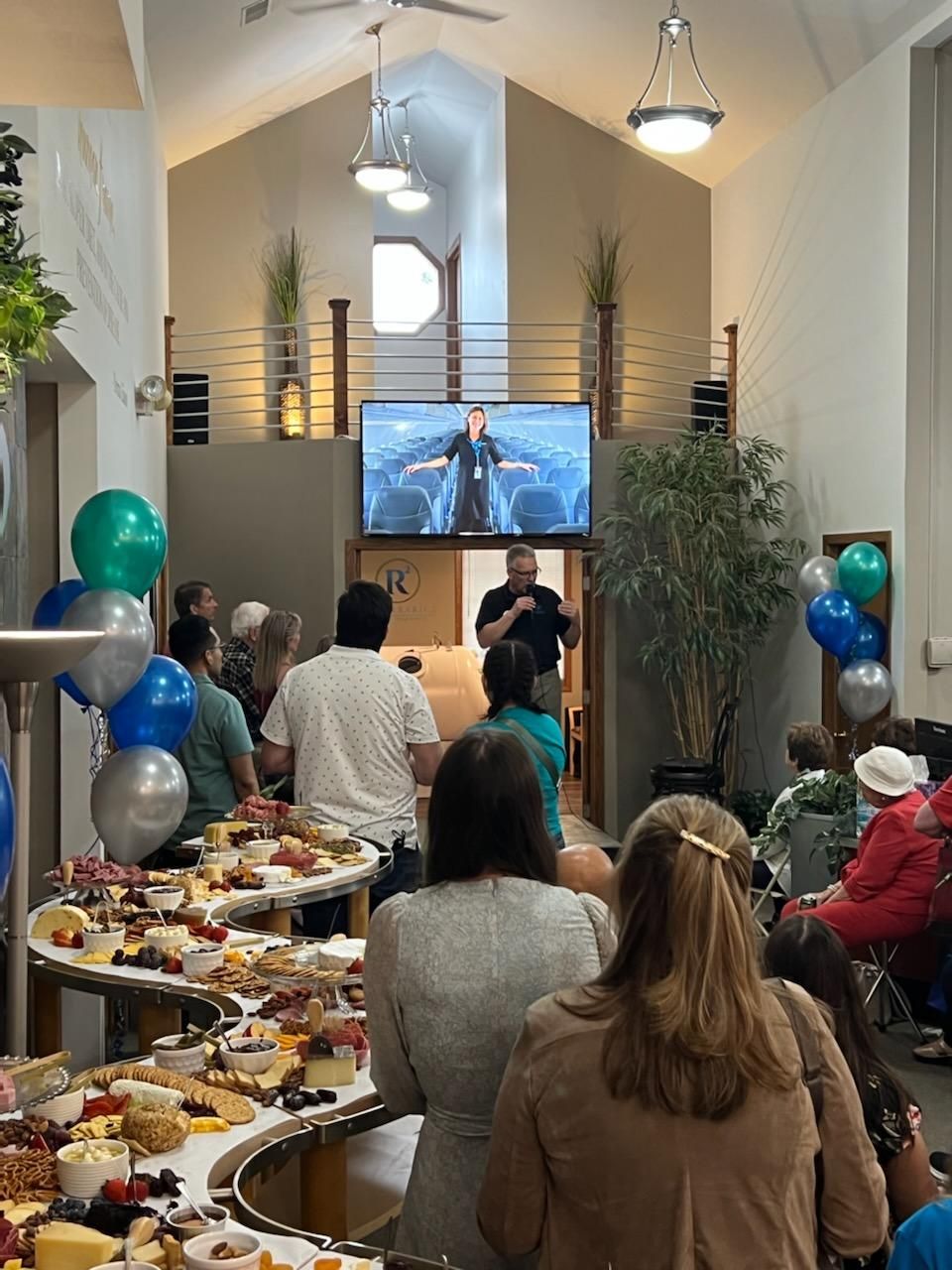 A group of people are sitting in a room with tables of food and balloons.