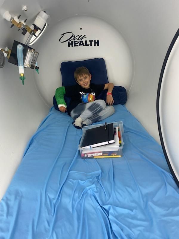 A boy is laying on a bed in an oxygen chamber